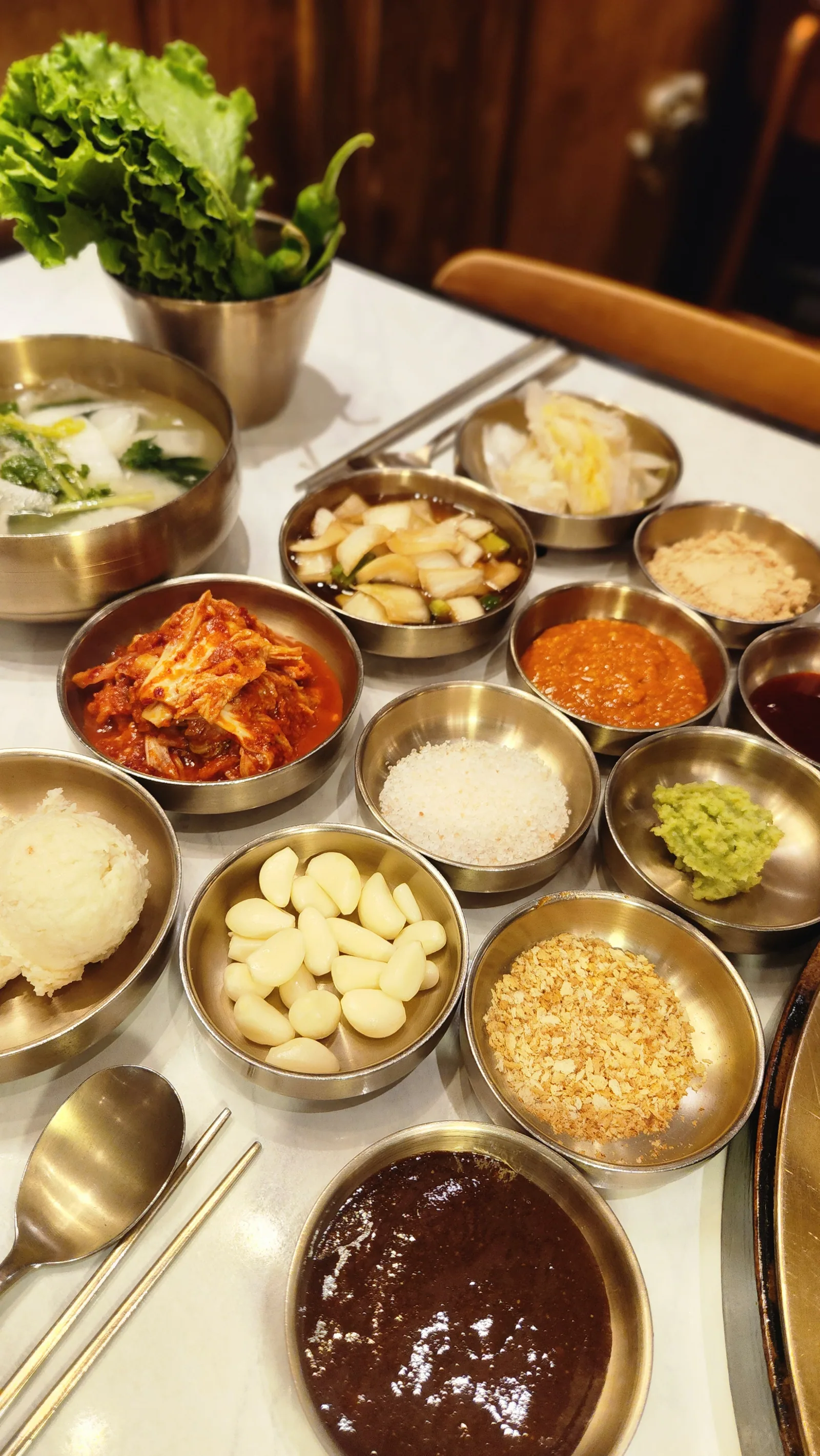 Banchan portioned into brass bowls — ssamjang, roasted soybean powder, kimchi, pickled vegetables and whole garlic