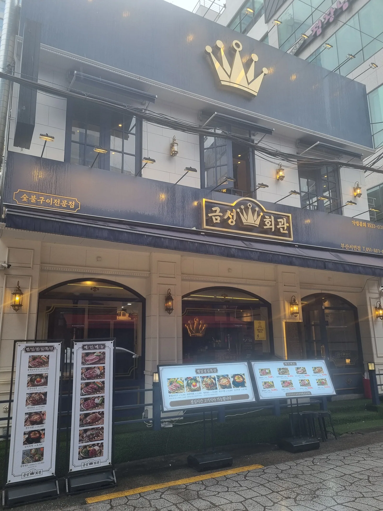 Angled view of Geumseong Hoegwan Seomyeon — charcoal grill house awning and brass lantern sconces