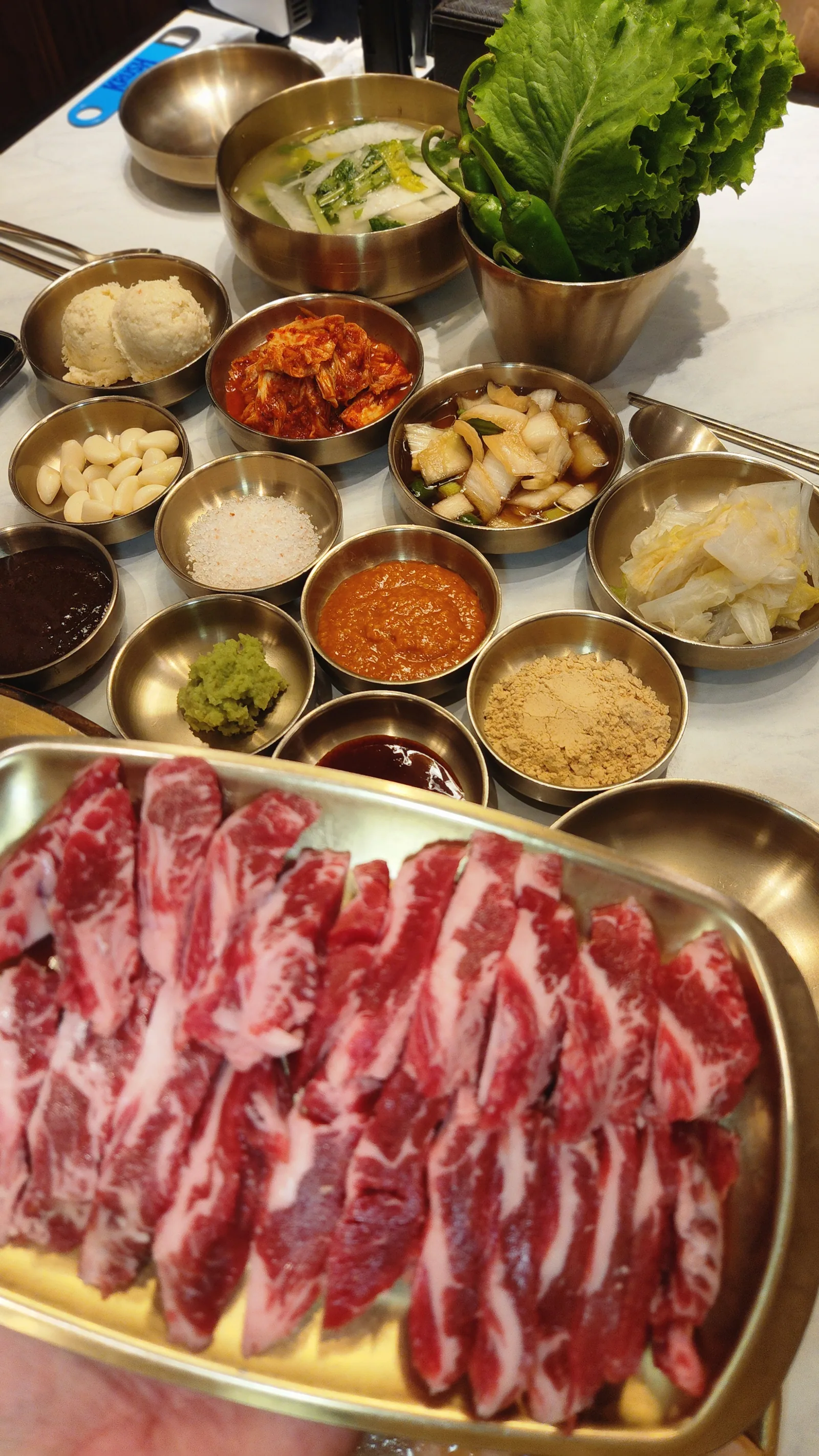 A full table of brassware banchan with raw meat on a brass tray